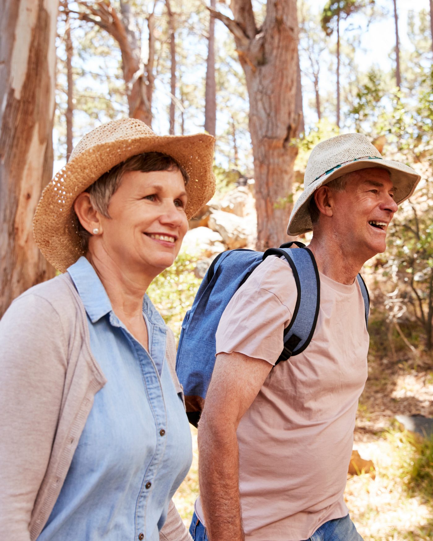 A couple in their sixties walking a wooded trail on a sunny day